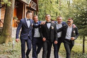 Cheerful, young, energetic witnesses of the groom next to the groom. Friends congratulate the groom. Groom and his funny friends having fun on the wedding day of the newlyweds. photo