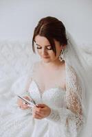 fashion photo of a beautiful bride with dark hair in an elegant wedding dress and stunning makeup in the room on the morning of the wedding. The bride is preparing for the wedding