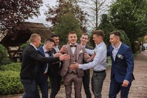 Cheerful, young, energetic witnesses of the groom next to the groom. Friends congratulate the groom. Groom and his funny friends having fun on the wedding day of the newlyweds. photo