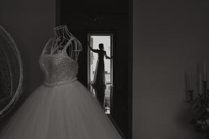 A happy bride is preparing for her luxurious wedding in a hotel room, with a wedding dress on a mannequin nearby. Portrait of a woman with fashionable hair, makeup and a smile in a dressing gown. photo