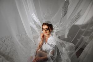 Nice cute girl in a boudoir robe. Happy beautiful bride under veil. Fashion, beauty, style. Morning of the bride. Beautiful bride with stylish make up and hair style. photo