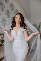 A wonderful beautiful portrait of a young bride. Beautiful bride with wedding makeup and jewelry wreath on long curly hair. Wedding photo model with brown eyes in a beautiful interior.