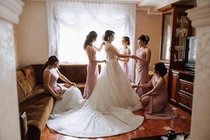 Friends rejoice with the bride in the morning. They take pictures, smile, help the bride fasten her dress. photo