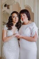 A beautiful and happy mother and her daughter, the bride, are standing next to each other. The best day for parents. Tender moments at the wedding. photo