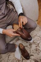 un elegante hombre usa marrón cuero formal zapatos. atadura zapatos. negocio hombre atadura cordones de los zapatos en el piso. arriba cerca el novio es preparando para el boda. foto