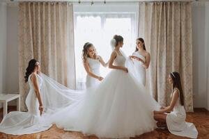 Friends rejoice with the bride in the morning. They take pictures, smile, help the bride fasten her dress. photo