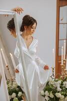 portrait of a luxurious bride in boudoir style near a mirror with reflection. Preparing the bride for the wedding in the morning in a white robe. photo