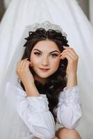 A beautiful brunette bride with a tiara in her hair is getting ready for the wedding in a beautiful robe in boudoir style. Close-up wedding portrait, photo. photo