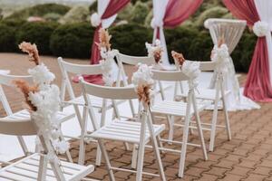 Boda decoración. muchos blanco sillas y un blanco camino. un blanco y rosado arco decorado con flores preparación para el Boda ceremonia. celebracion foto