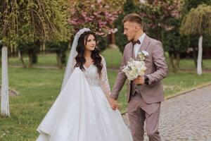 Portrait of a young bride and groom walking through the garden after the wedding ceremony. The bride and groom are walking in a beautiful spring blooming park. Happy wedding couple, copy space photo