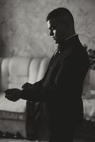 el novio sujeta el botón en el chaqueta de el del novio Mañana reuniones preparando el novio para el boda. negro y blanco foto. foto