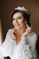 A beautiful brunette bride with a tiara in her hair is getting ready for the wedding in a beautiful robe in boudoir style. Close-up wedding portrait, photo. photo