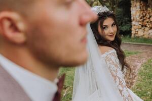 A handsome groom in the spring forest stands in front of his bride. Beautiful wedding white dress. Walks in the park. A happy and loving couple. photo