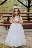 pequeño rubio niña con flores en su cabeza, en un blanco vestido, participación Boda anillos para el Boda ceremonia. primavera Boda foto