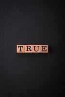 The inscription True made of wooden cubes on a plain background photo