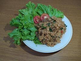 delicioso indonesio frito arroz nasi goreng con un montón de lechuga, mostaza verduras y Tomates servido en un blanco plato foto