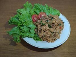 delicioso indonesio frito arroz nasi goreng con un montón de lechuga, mostaza verduras y Tomates servido en un blanco plato foto