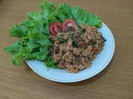 Delicious Indonesian fried rice nasi goreng with lots of lettuce, mustard greens and tomatoes served on a white plate photo