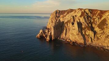 aereo Visualizza scogliere mare dove montagne incontrare oceano panoramico Visualizza illuminata dal sole scogliere mare scintillante sotto. scogliere Torre al di sopra di mare in mostra selvaggio bellezza maestoso aereo visualizzazioni intatto natura selvaggia. video