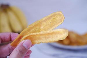 Hand holding banana chips on white background with copy space. Selective focus. photo