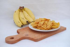 Crispy banana chips on a white plate with fresh bananas. photo