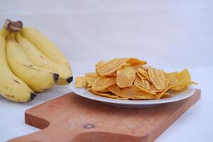 Crispy banana chips on a white plate with fresh bananas. photo