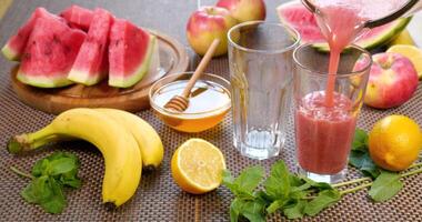 Watermelon banana Smoothie is poured into a glass on the background of fresh fruits. The fruit cocktail is ready to eat. Healthy and vegetarian food concept. Ultra 4K video