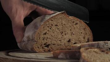 Cutting slice of homemade Crusty rye bread with a sharp knife on wooden board, closeup slow motion video