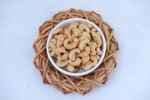 Roasted cashew nuts in white bowl on bamboo mat, stock photo