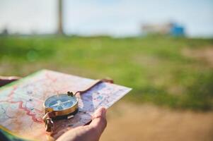 Close-up tourist's hand holds compass with magnetic arrow showing north direction, over map against lighthouse backdrop photo