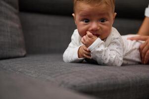 Close-up portrait of a cute baby boy lying on his tummy while his loving mom changing nappy on the couch at home photo