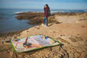 detalles en un Brújula y mapa en un rock en contra borroso hembra turista mirando dentro el distancia mediante prismáticos foto