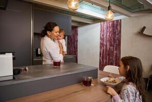 Portrait of a happy family, a single mother with two kids during breakfast in the morning at home kitchen photo