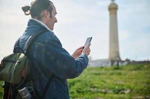 Young adult man traveler tourist hiker adventurer checks mobile application on his smartphone while exploring the nature photo