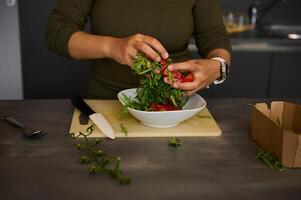 Hands holding fresh green arugula leaves and juicy red tomatoes while preparing healthy raw vegan salad in home kitchen photo