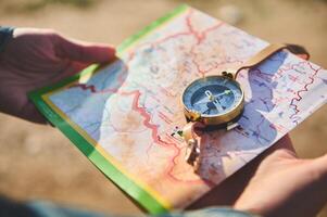 Close-up of traveler's hands holding map and using compass, searching direction while hiking, exploring nature photo