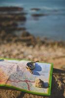 Close-up of an old golden compass and geographic map on a rock over seascape background. Trip. Tourism. Travel concept. photo