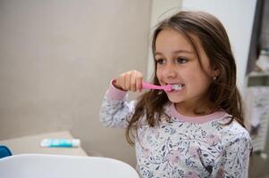 caucásico niño niña cepillado su dientes en el baño. oral cuidado y dental higiene a evitar caries y diente decaer foto