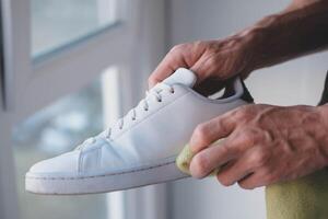 un hombre limpia blanco zapatillas desde suciedad foto