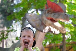 un niño carcajadas a el visión de un dinosaurio. Adolescente chico en dinoparque. foto