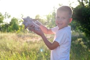 pequeño chico corriendo con un juguete cohete en un puesta de sol campo de verano naturaleza. para niños grande sueño, vuelo, astronauta, espacio, éxito líder ganador concepto foto