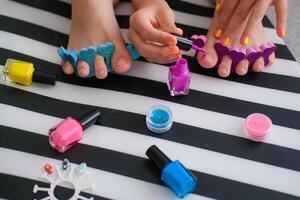 Children's feet with bright pedicure and manicure of different colors and bottles of bright nail polish. Little girl does a pedicure. Beauty salon game. Children's entertainment. photo