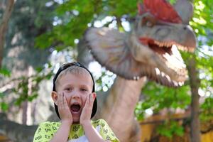 un niño carcajadas a el visión de un dinosaurio. Adolescente chico en dinoparque. foto