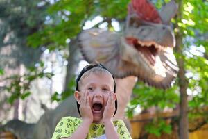 un niño carcajadas a el visión de un dinosaurio. Adolescente chico en dinoparque. foto