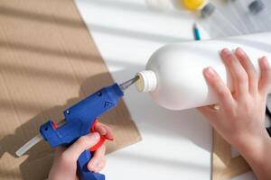 Step-by-step instructions for making crafts from improvised materials. Handmade at school craft rocket for the day of cosmonautics. A child smears a plastic bottle with glue. Step 2 photo