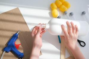 paso a paso instrucciones para haciendo artesanía desde improvisado materiales hecho a mano a colegio arte cohete para el día de cosas de cosmonautas. el niño es pegar partes a un el plastico botella. paso 3 foto