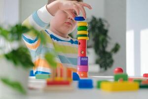 un pequeño chico obras de teatro con de madera juguetes y construye un torre. educativo lógica juguetes para niños. montessori juegos para niño desarrollo. para niños de madera juguete. foto