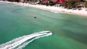 Aerial view of white sand beach and jet ski on the blue lagoon aqua sea. Aerial bird's eye view of jet ski cruising in high speed in turquoise clear water sea video