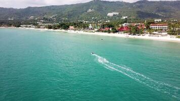 Aerial view of white sand beach and jet ski on the blue lagoon aqua sea. Aerial bird's eye view of jet ski cruising in high speed in turquoise clear water sea video