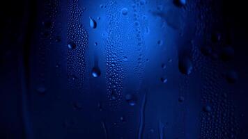 A drop of water on a glass close-up macro with sparkling bokeh on blue blurred background. Abstract drop water. Raindrop slide down the window glass, forming abstract figure video